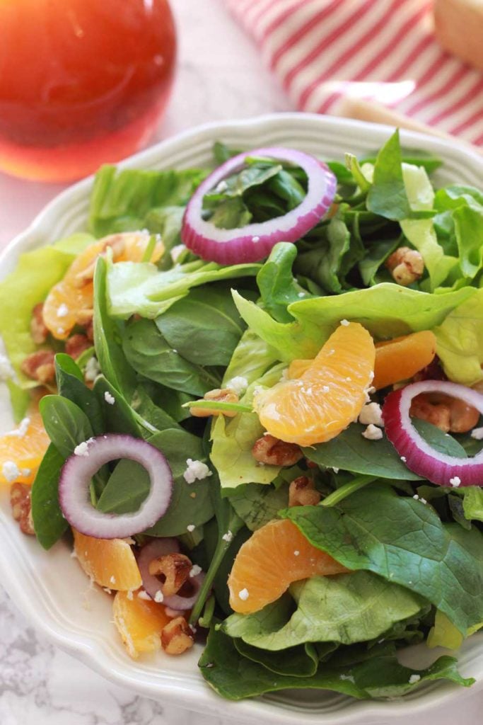 A close up of a green salad topped with red onions, walnuts and goat cheese crumbles.