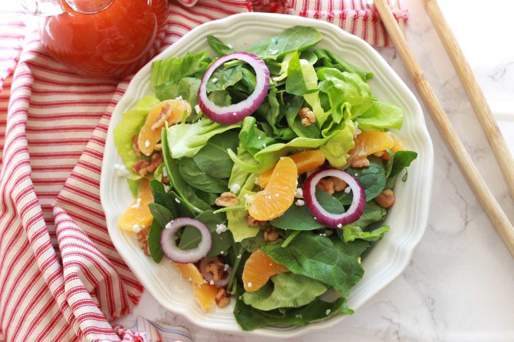 A plate of a green salad topped with red onions, walnuts and goat cheese crumbles.