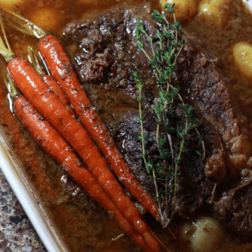 Baking dish filled with pot roast, baby potatoes, and carrots.