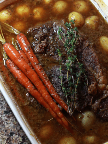 Baking dish filled with pot roast, baby potatoes, and carrots.