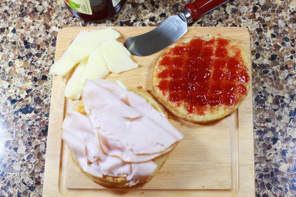 Brown cutting board with waffles, cheese, turkey and raspberry jam being used to make a Monte Cristo.