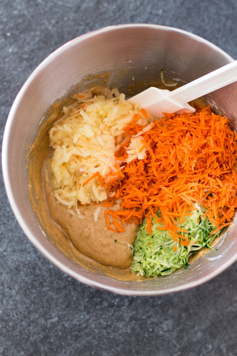 Silver bowl containing shredded apple, carrots, zucchini, and batter.
