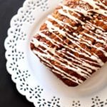 Zucchini, Carrot and Apple Olive Oil Cake topped with cream cheese frosting sitting on a white lace plate.