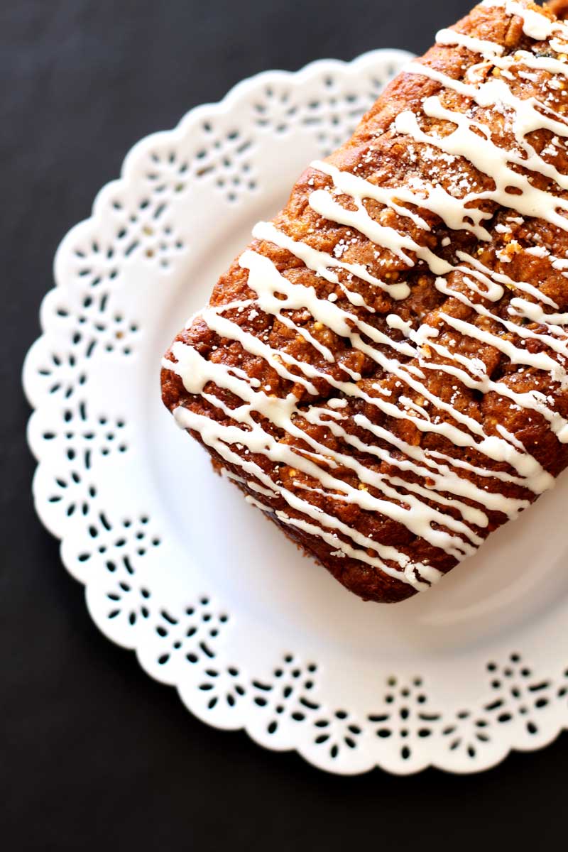 Zucchini Carrot Bread topped with cream cheese frosting sitting on a white lace plate.