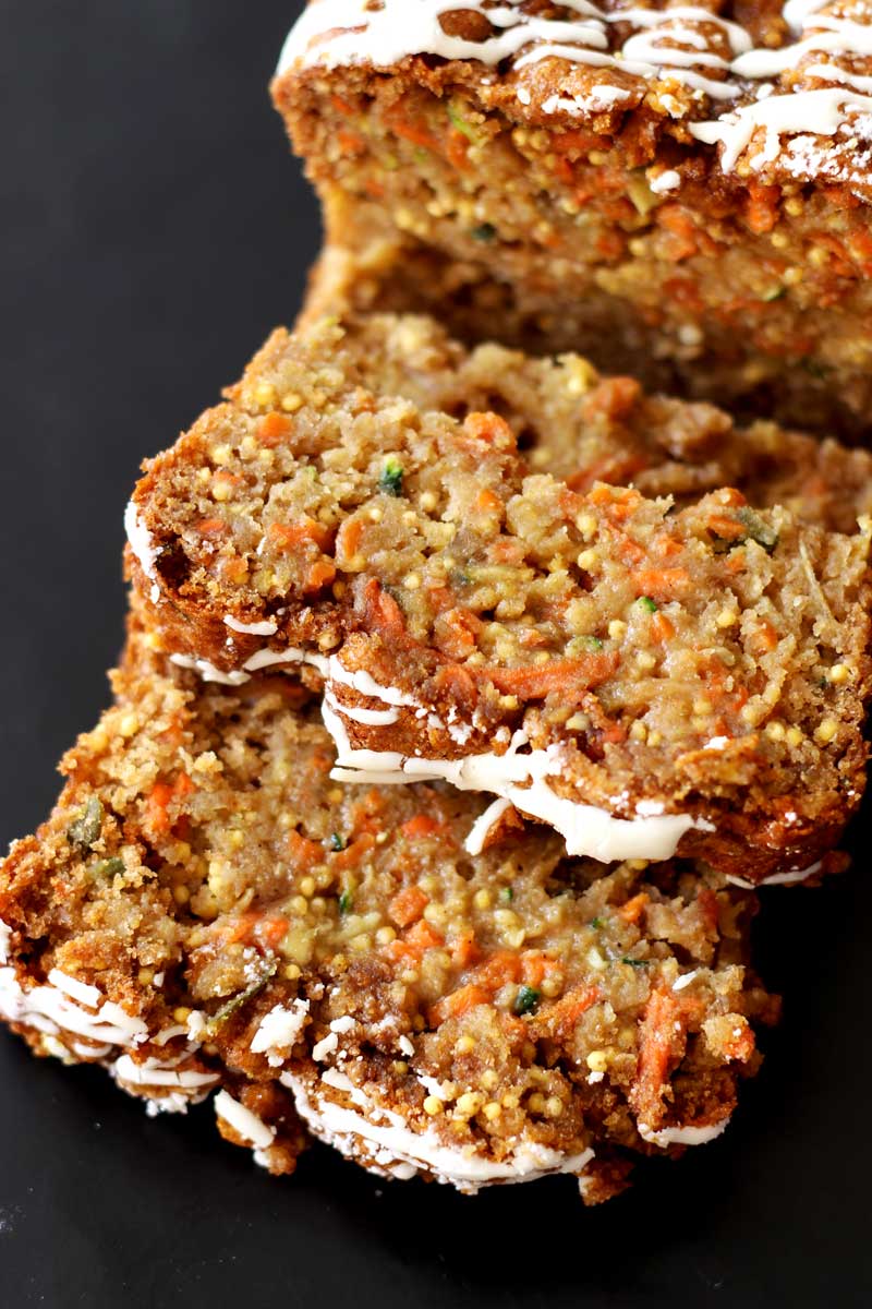 Sliced Zucchini, Carrot and Apple Olive Oil Cake topped with cream cheese sitting on a black table.