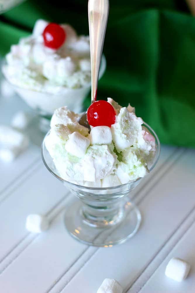 Parfait glass filled with Pineapple Pistachio Marshmallow Dessert topped with a cherry, spoon in parfait glass.