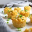 Six macaroni and cheese bites sitting on a white table, topped with chives.
