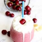 A close up of glass filled with smoothie topped with whipped cream and a cherry.