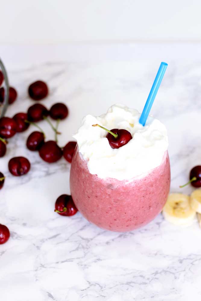 A close up of a cherry smoothie topped with whipped cream and a cherry.