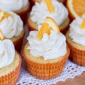 Nine Orange Creamsicle Cupcakes sitting on a white lace napkin topped with vanilla frosting and topped with orange slice.