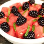 White bowl containing cubed watermelon and blackberries, topped with fresh mint.