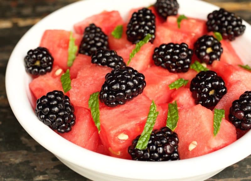 White bowl containing cubed watermelon and blackberries, topped with fresh mint.