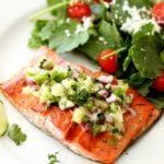 Filet of salmon topped with cucumber lime salsa, salad on side.