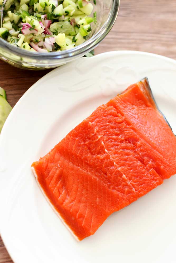 Filet of Raw Sockeye Salmon sitting on a white plate, cucumber lime salsa in bowl.