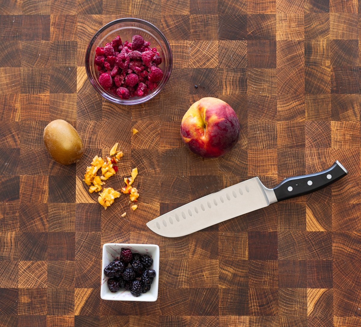 Person chopping raspberries, kiwi, peaches, and blackberries.
