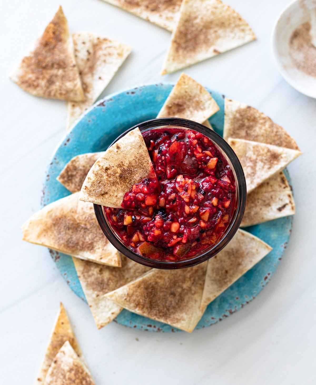 Plate filled with cinnamon chips and person dipping it in a container of fruit salsa.