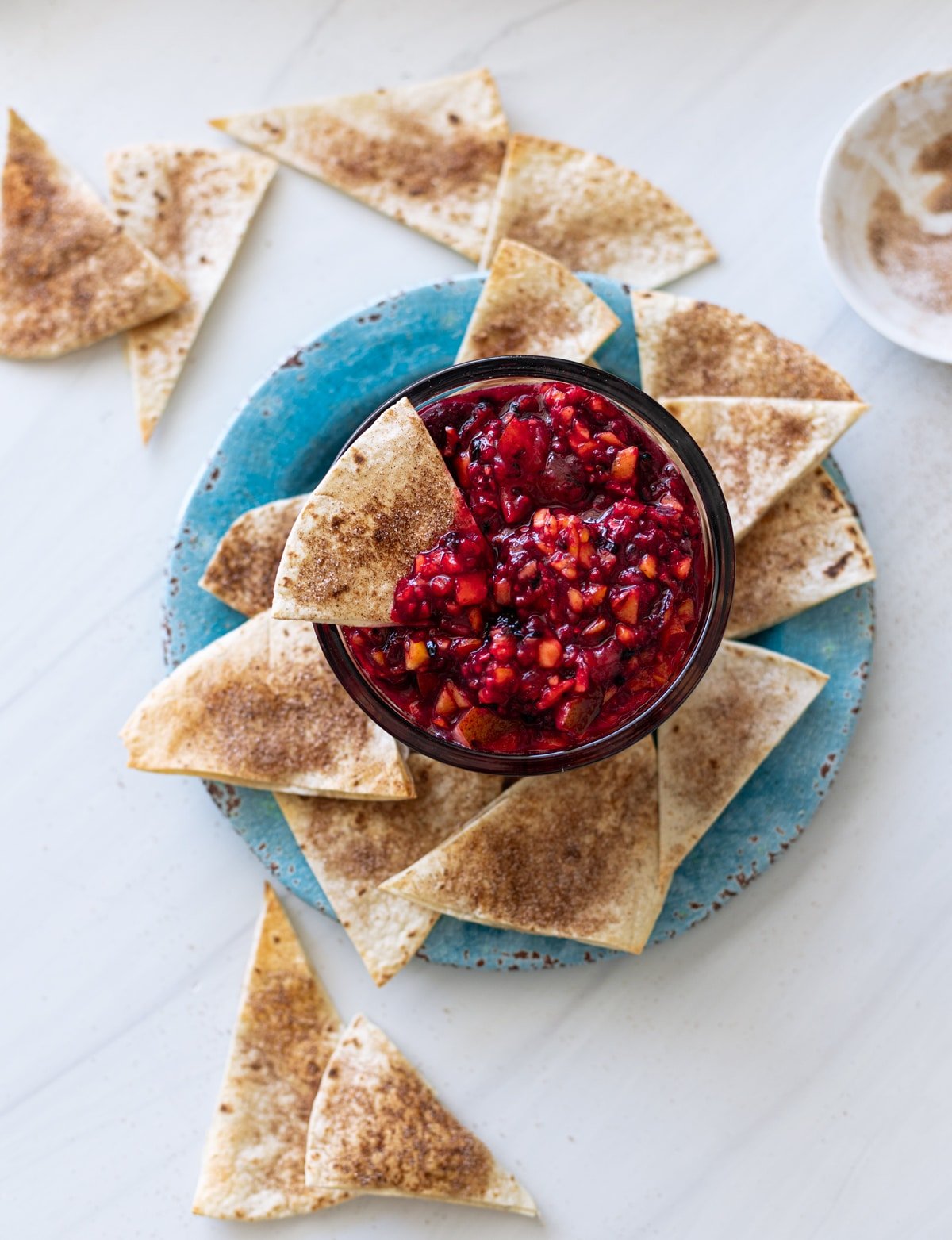 Bowl of fruit salsa being eaten with a cinnamon sugar chip.