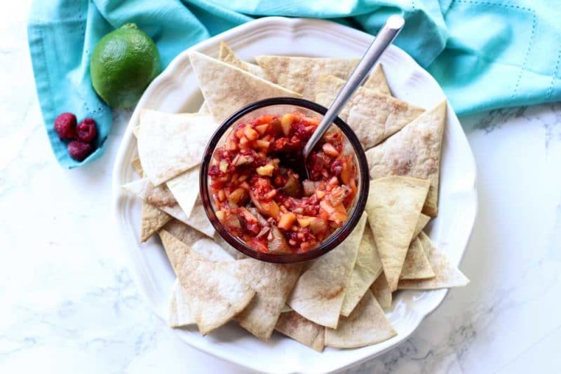 A close up of tortilla chips and salsa with a spoon in the salsa

