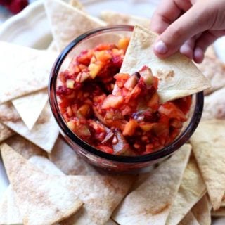 A person dipping salsa with a tortilla chip from a bowl