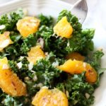 A close up of a plate of orange and kale salad with a fork