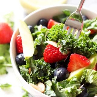 White bowl containing Apple and Berry Chopped Kale Salad, fork containing strawberry, kale and almond.