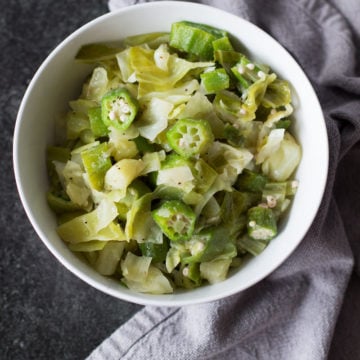 White bowl containing cabbage and okra on black granite counter.