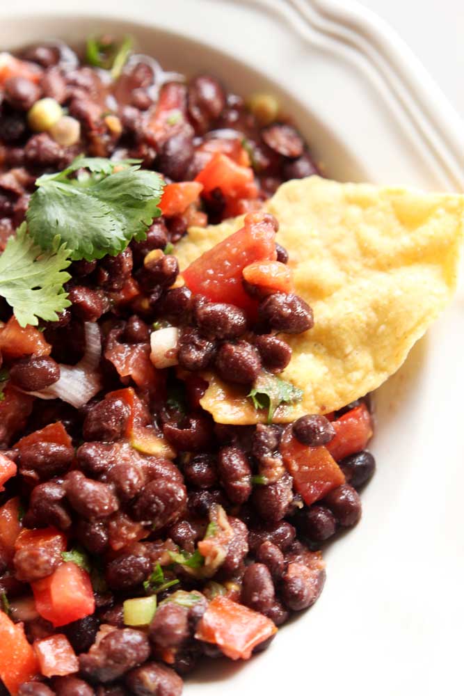 White bowl containing a black bean dip topped with cilantro, tortilla chip in dip.