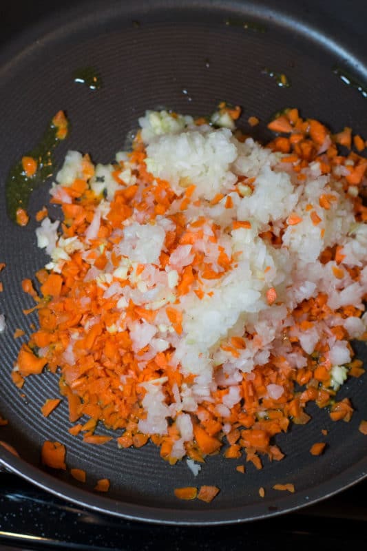 Skillet containing shredded carrots, garlic, and onion.