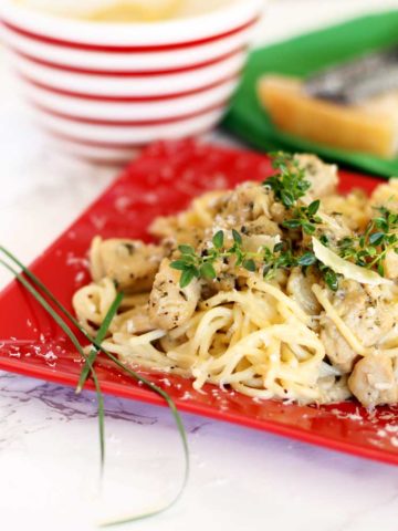 Red plate containing Garlic Basil Chicken Pasta topped with fresh thyme and Parmesan cheese.