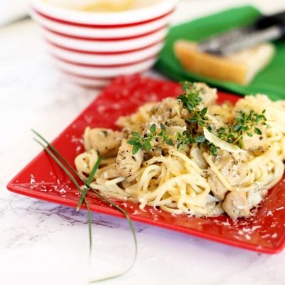 Red plate containing Garlic Basil Chicken Pasta topped with fresh thyme and Parmesan cheese.