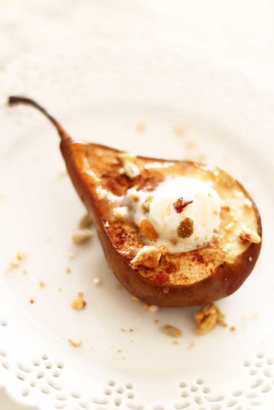 Baked pear topped with granola and ice cream, sitting on a white plate.