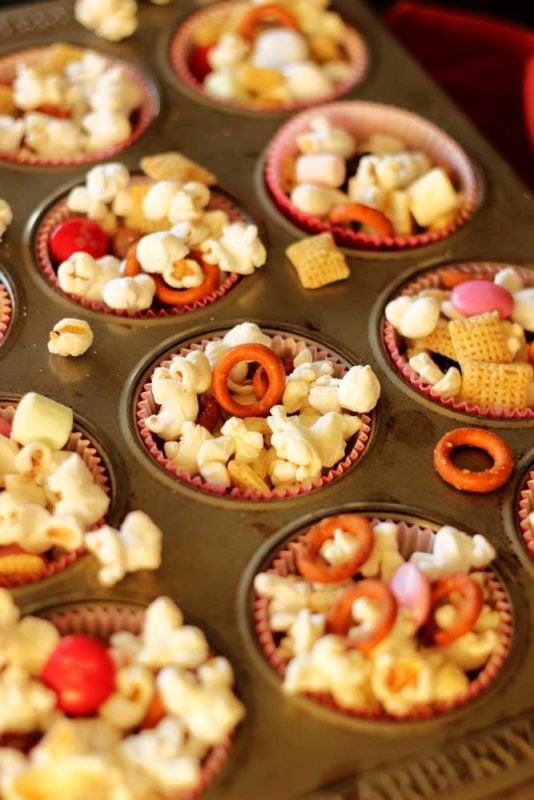 Cupcake tin filled with a popcorn snack containing popcorn, pretzels and M&Ms.