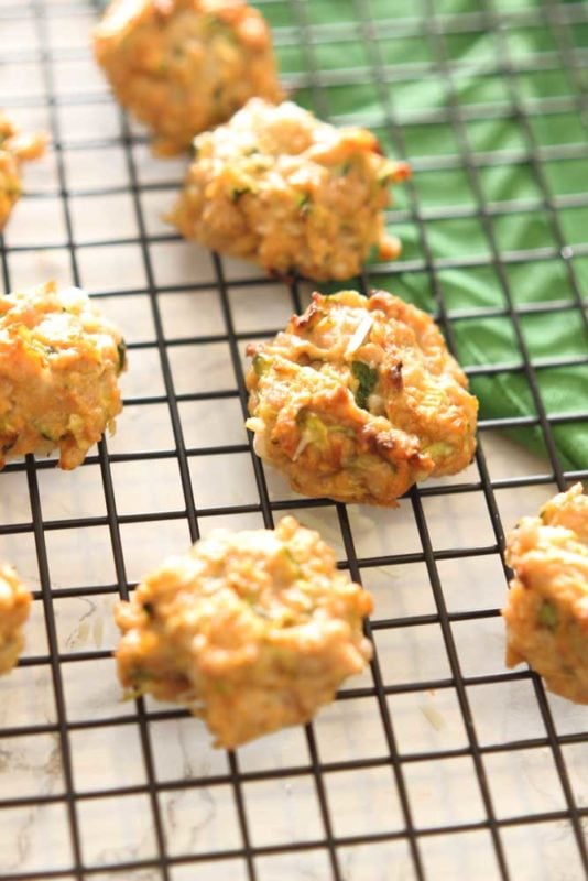 7 Chicken Zucchini Bites sitting on a black wire cooling rack, green napkin on table.