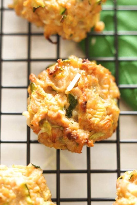 A zucchini chicken bite sitting on a black wire cooling rack, topped with Parmesan Cheese.