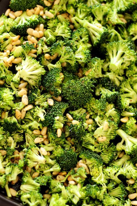Sheet pan containing broccoli spears with pine nuts and fresh ground pepper.