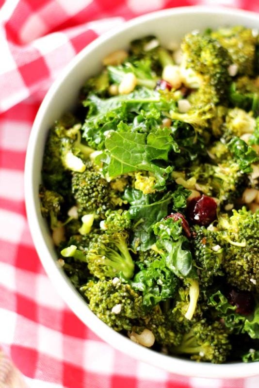 White bowl containing a kale and broccoli salad sitting on a red and white gingham napkin.