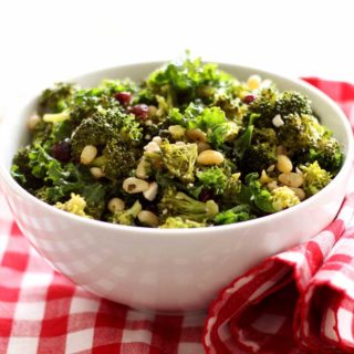 White bowl containing broccoli and kale salad with pine nuts and feta cheese on top, sitting on a red and white gingham napkin.