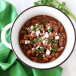 Pinto Beans in a white bowl sitting on a white table with a green napkin topped with feta cheese and fresh parsley.