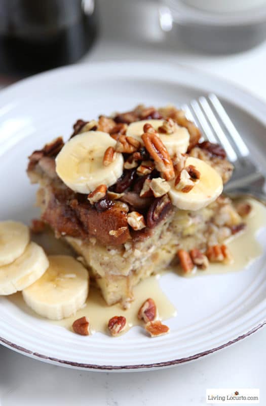 A white plate with french toast, sliced bananas topped with pecans, silver fork.