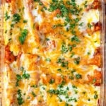 Pyrex dish of cheesy chicken enchiladas topped with fresh parsley.