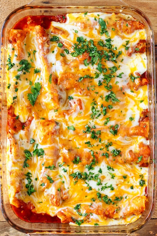 Pyrex dish of cheesy chicken enchiladas topped with fresh parsley.