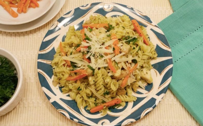 Rotini pasta topped with chicken, carrots and Parmesan cheese, in a blue and white plate on a white table.