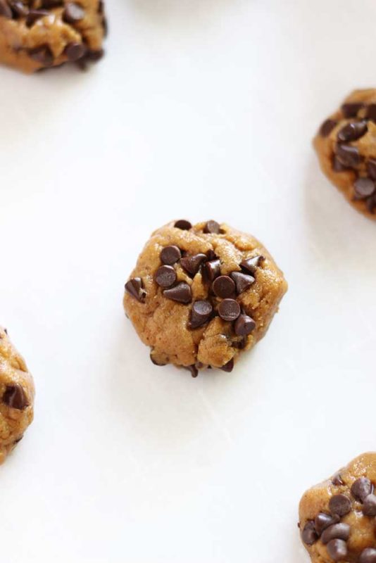 Raw chocolate chip cookie dough ball sitting on a cookie sheet lined with Parchment paper.