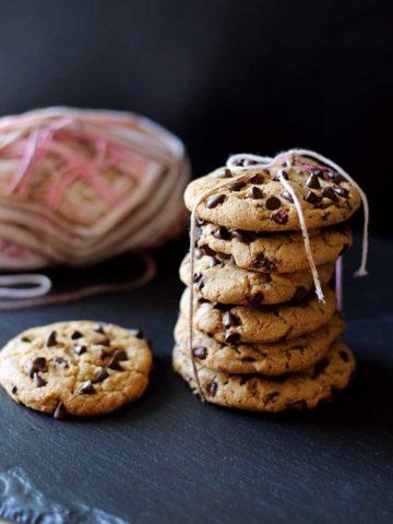6 chocolate chip cookies tied with pink yarn sitting on a black slate, 1 cookie beside package of cookies.