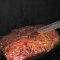 Seasoned Barbecue Brisket sitting on a grill, baster with juice on brisket.