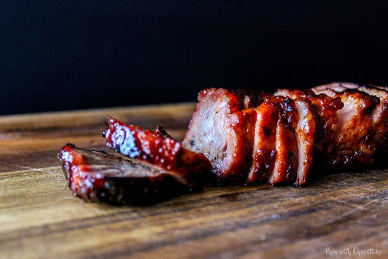 Sliced Sweet and Sticky Chinese BBQ Pork sitting on a wooden table topped with BBQ sauce.
