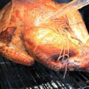 Traditional Smoked Turkey sitting on a grill, baster with juice.