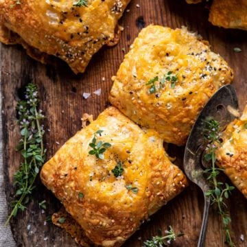 Four broccoli cheddar mini pies topped with fresh thyme on a cutting board.