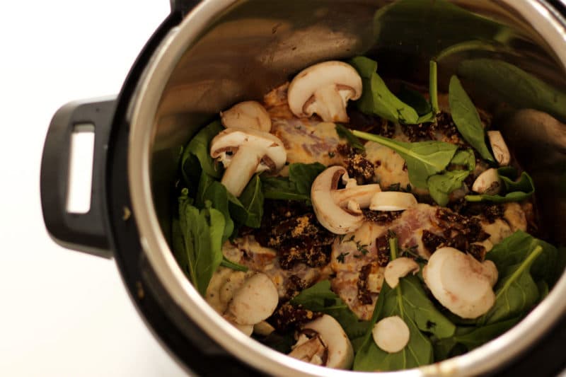 Instant Pot containing fresh mushrooms, spinach leaves chicken thighs and sun dried tomatoes.