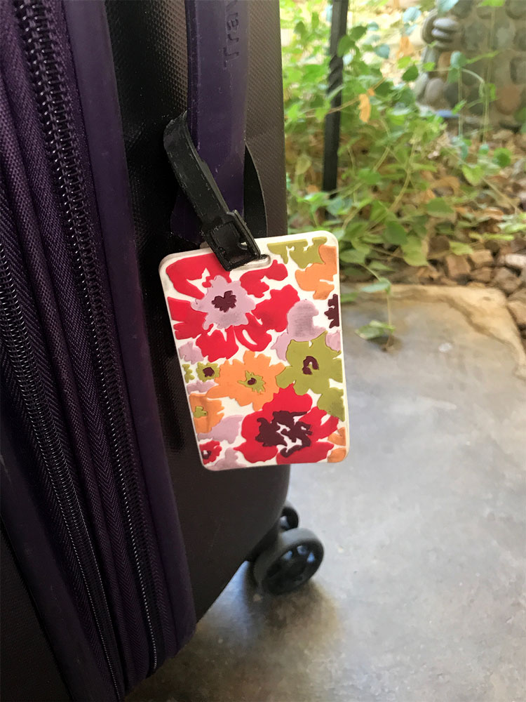 Hawaiian Obnoxious Luggage Tag attached to a purple suitcase featured in a gift guide for international travelers. 